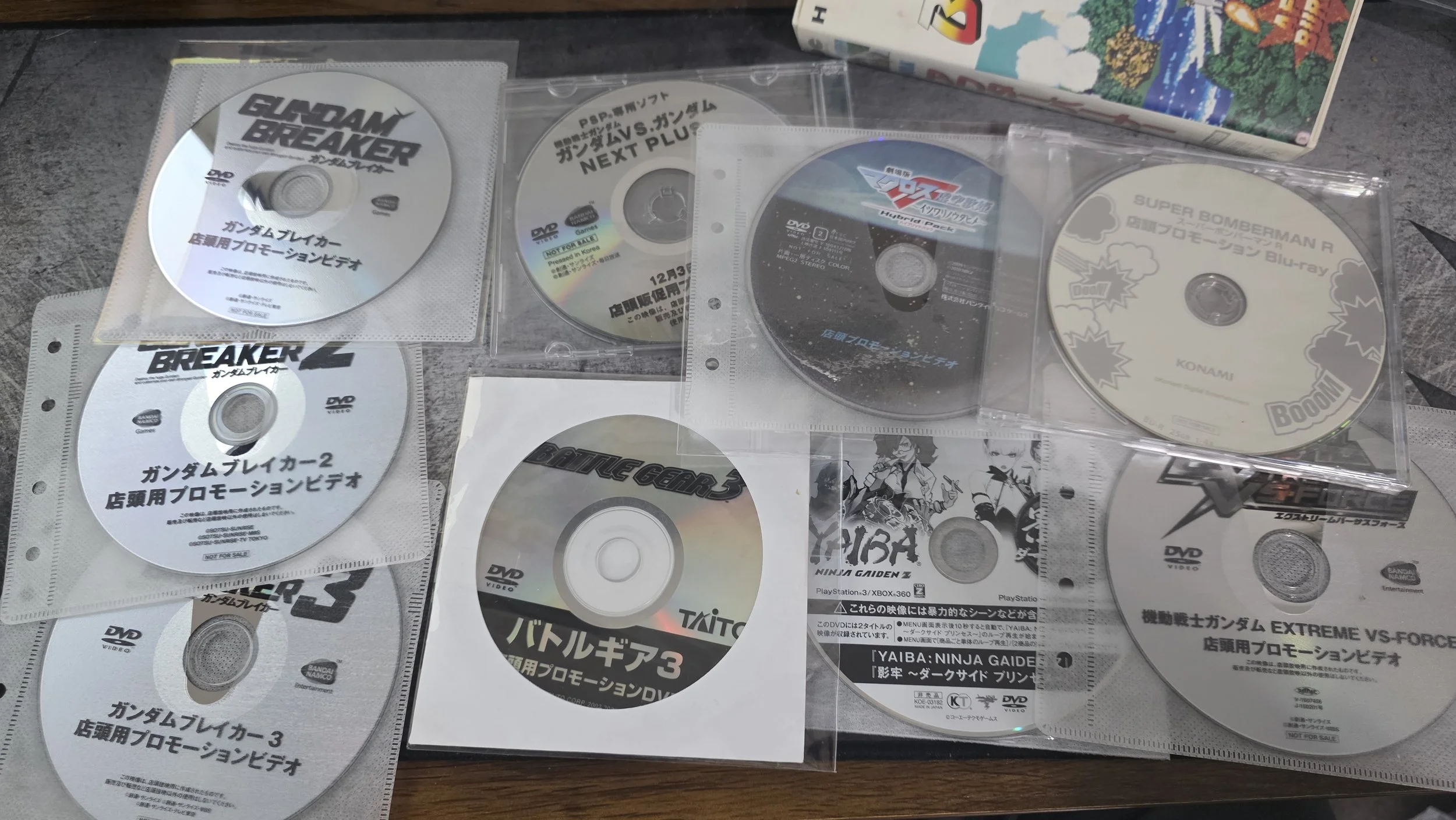 Multiple DVDs of Gundam and other mecha series, some in plastic sleeves, on a table with a nearby board game box.