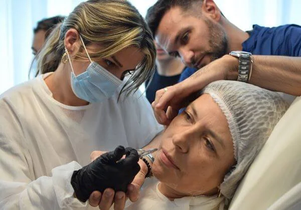 Médico realizando un procedimiento facial en una mujer mayor mientras otra profesional observa