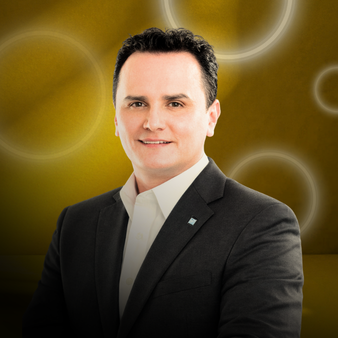 Hombre con blazer negro y camisa blanca sonriendo, fondo dorado con círculos brillantes.
