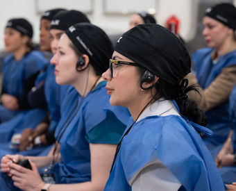 Grupo de enfermeros en capacitación con uniformes azules y gorros, en un entorno clínico.