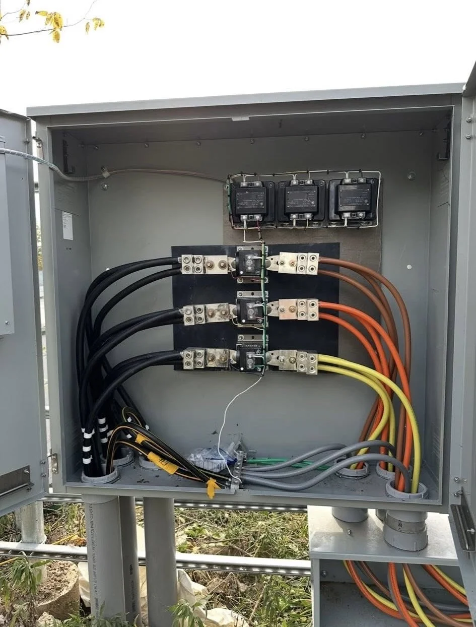 Electrical utility box with various wires, circuit breakers, and switches inside, mounted outdoors on a gray metal enclosure.
