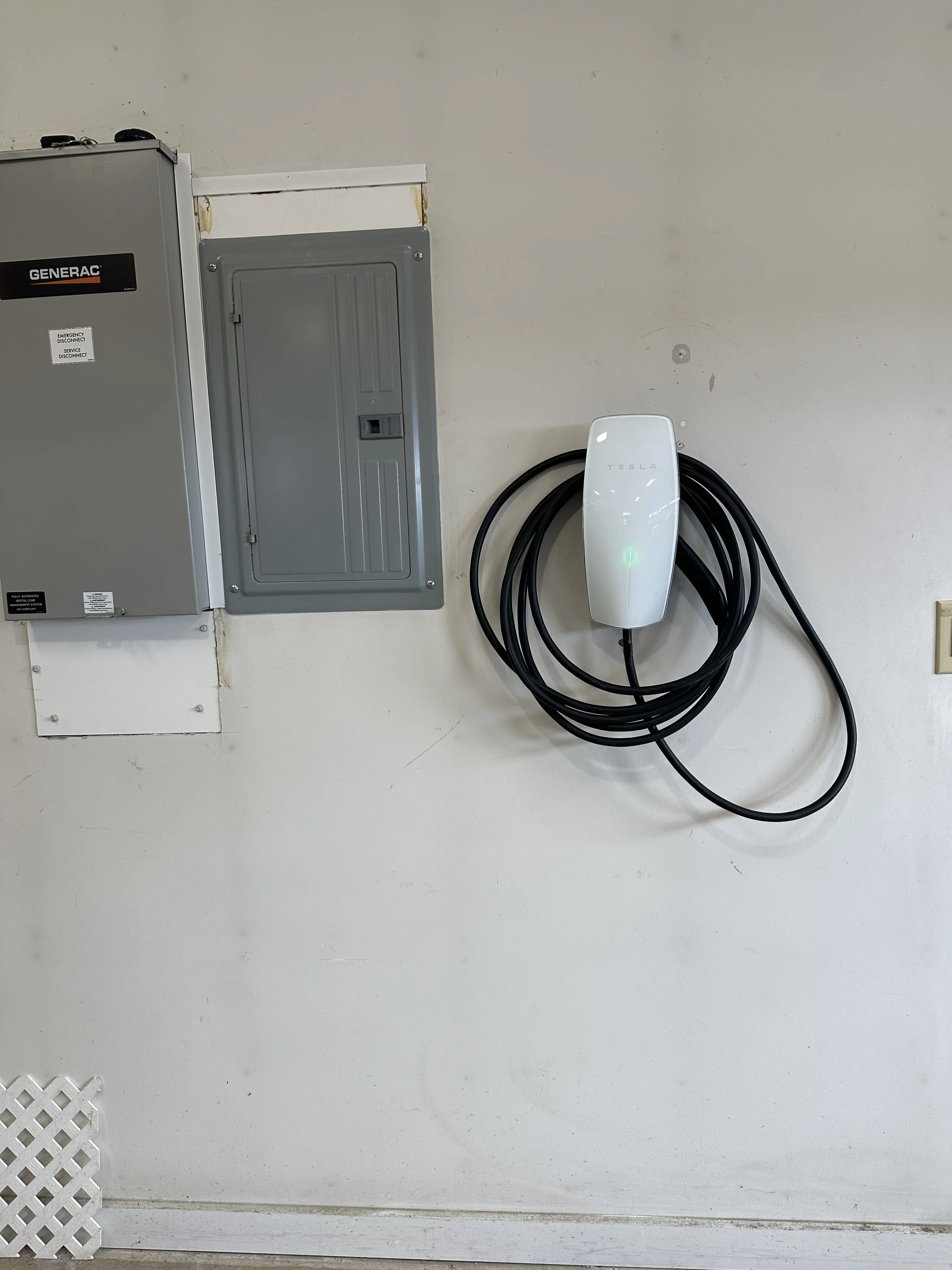 Electric vehicle charging station attached to a garage wall with a Tesla charger cable.