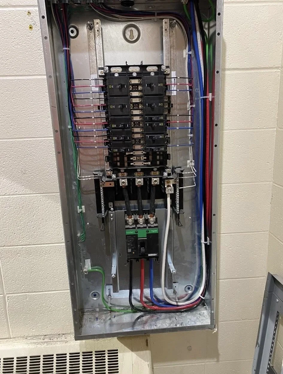 Open electrical breaker box with multiple circuit breakers, wires, and grounding connections inside.