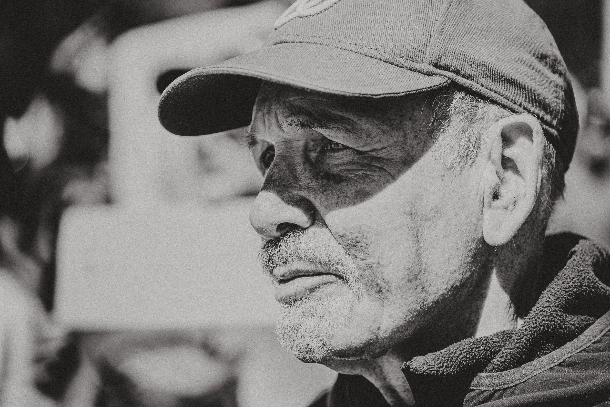 Close-up of an elderly man wearing a baseball cap, with a thoughtful expression, grayscale photograph