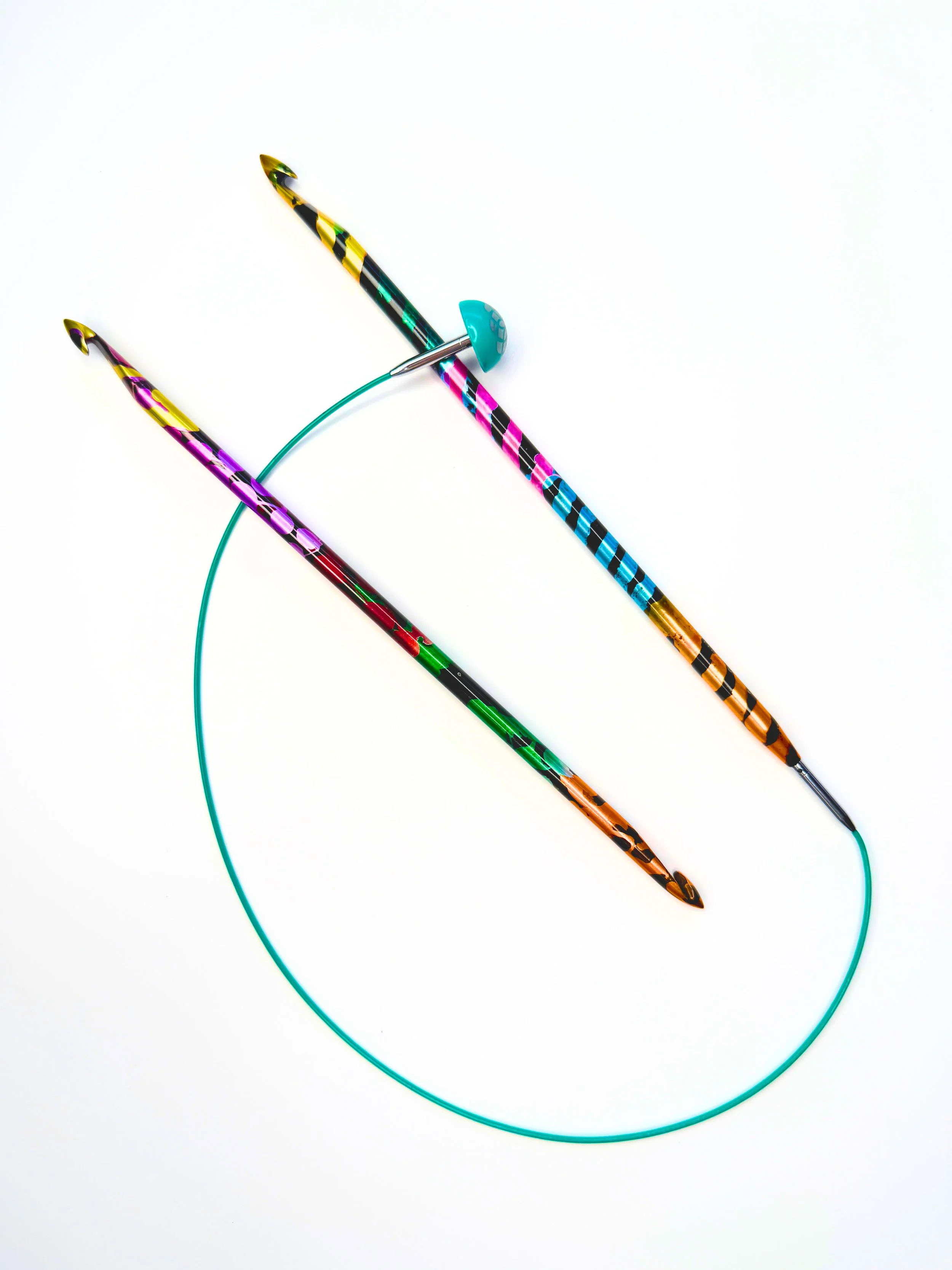 Two colourful, striped aluminium Tunisian crochet hooks connected by a turquoise flexible cable on a white surface.
