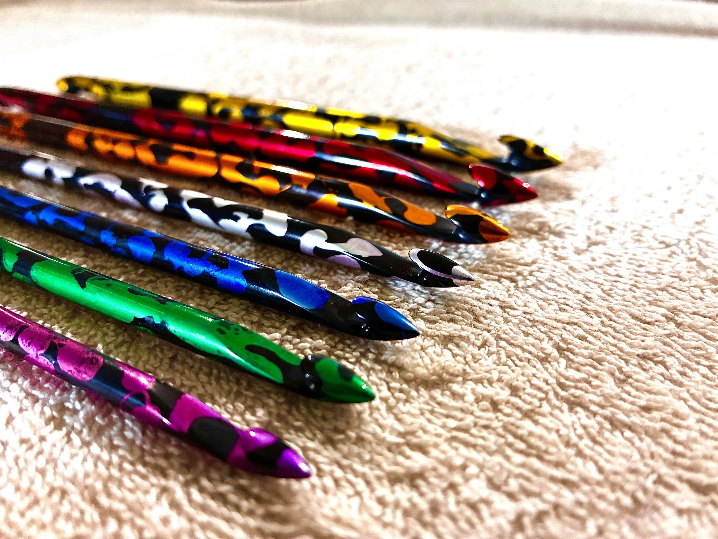 Colourful patterned Tunisian crochet hooks spread out on a beige carpet.
