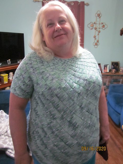 A smiling woman with shoulder-length blonde hair standing in a living room.