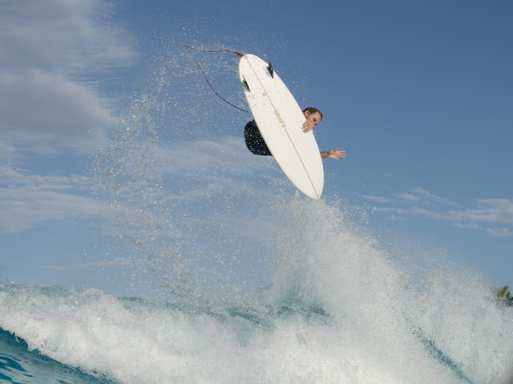 A person riding a wakeboard in the air above the water during daytime with a blue sky in the background.