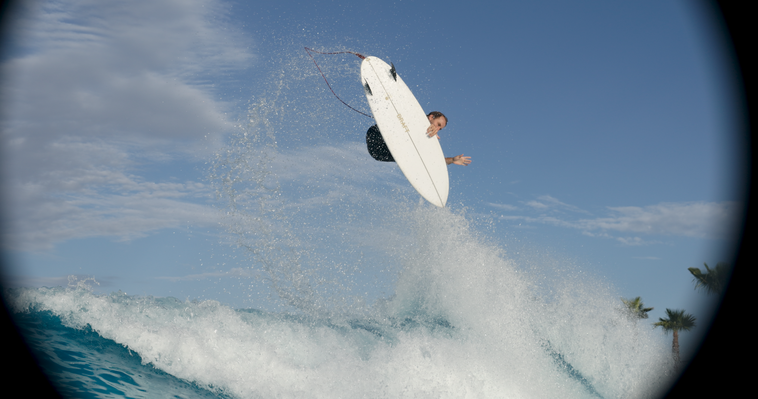 Person performing a jump on a surfboard above the ocean waves with a background of blue sky and scattered clouds.