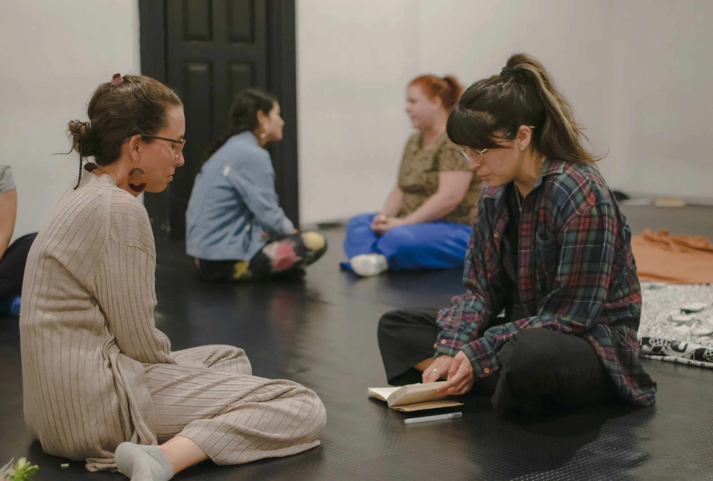 Grupo de cinco mujeres sentadas en el suelo en un espacio colaborativo, participando en una actividad de trabajo en equipo y liderazgo consciente.