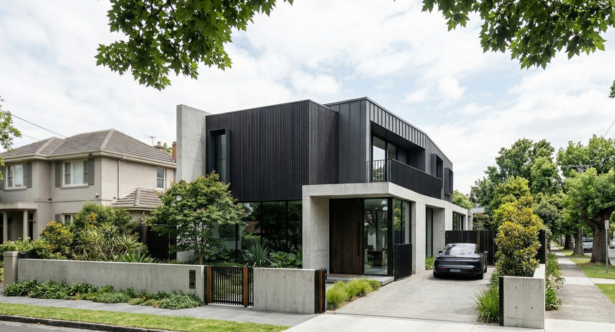Modern black and concrete residential building with a black car parked in front, surrounded by green trees and plants.