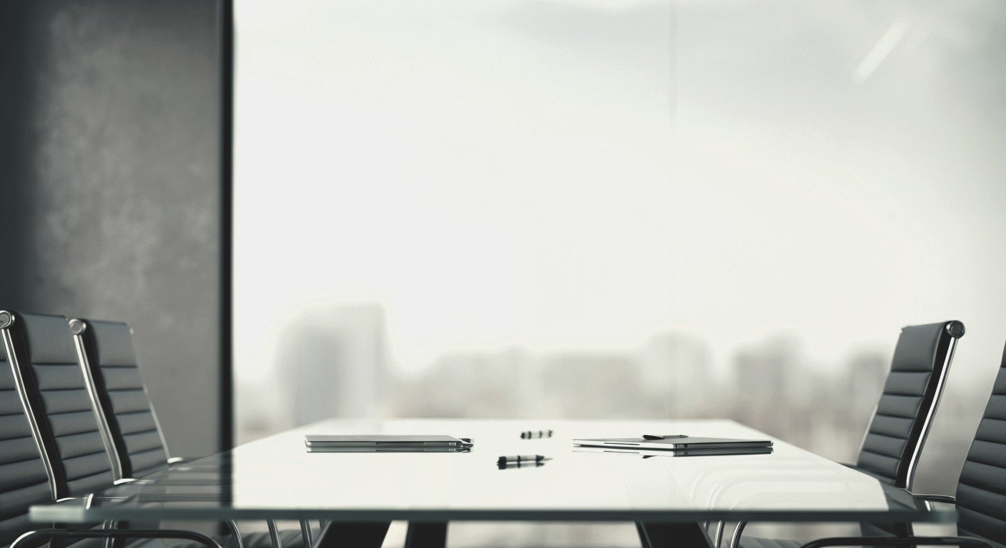 Mesa de reuniones de alta dirección vacía con computadoras portátiles y bolígrafos frente a un ventanal corporativo, simbolizando la autonomía operativa y la delegación en líderes empresariales.