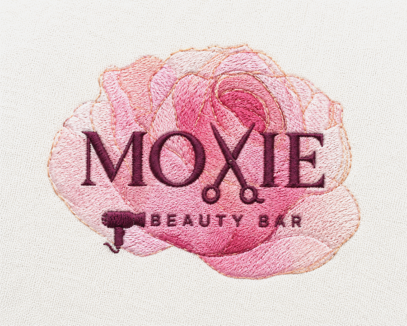 Embroidery patch for Moxie Beauty Bar featuring a pink rose with the word 'MOXIE' in bold purple embroidered text and scissors replacing the letter 'X'.