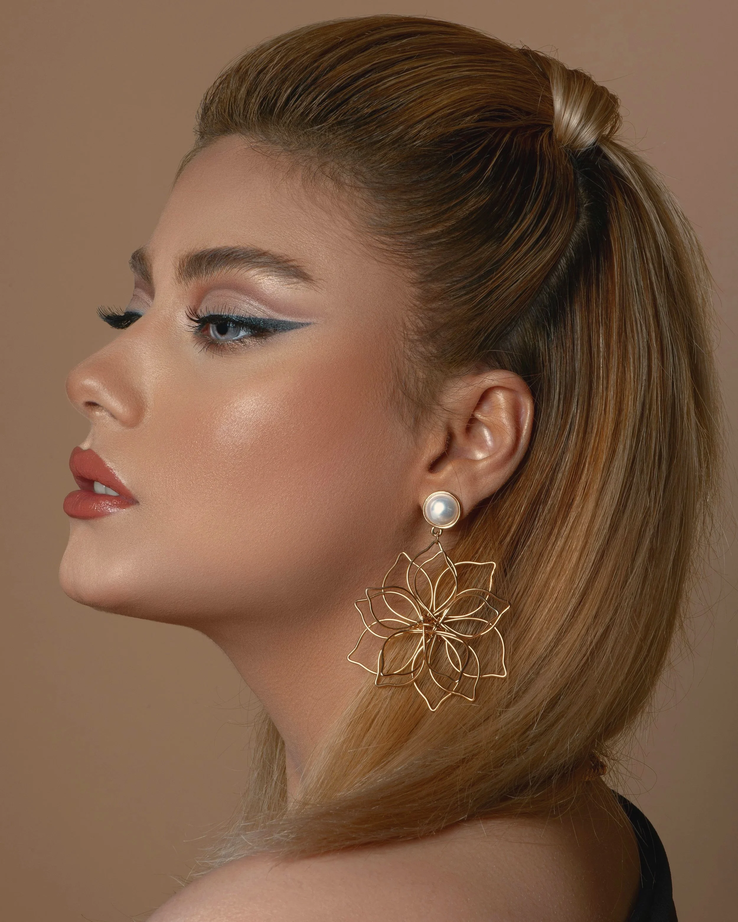 Close-up of a woman's face with makeup, styled hair, and a decorative earring shaped like a flower.