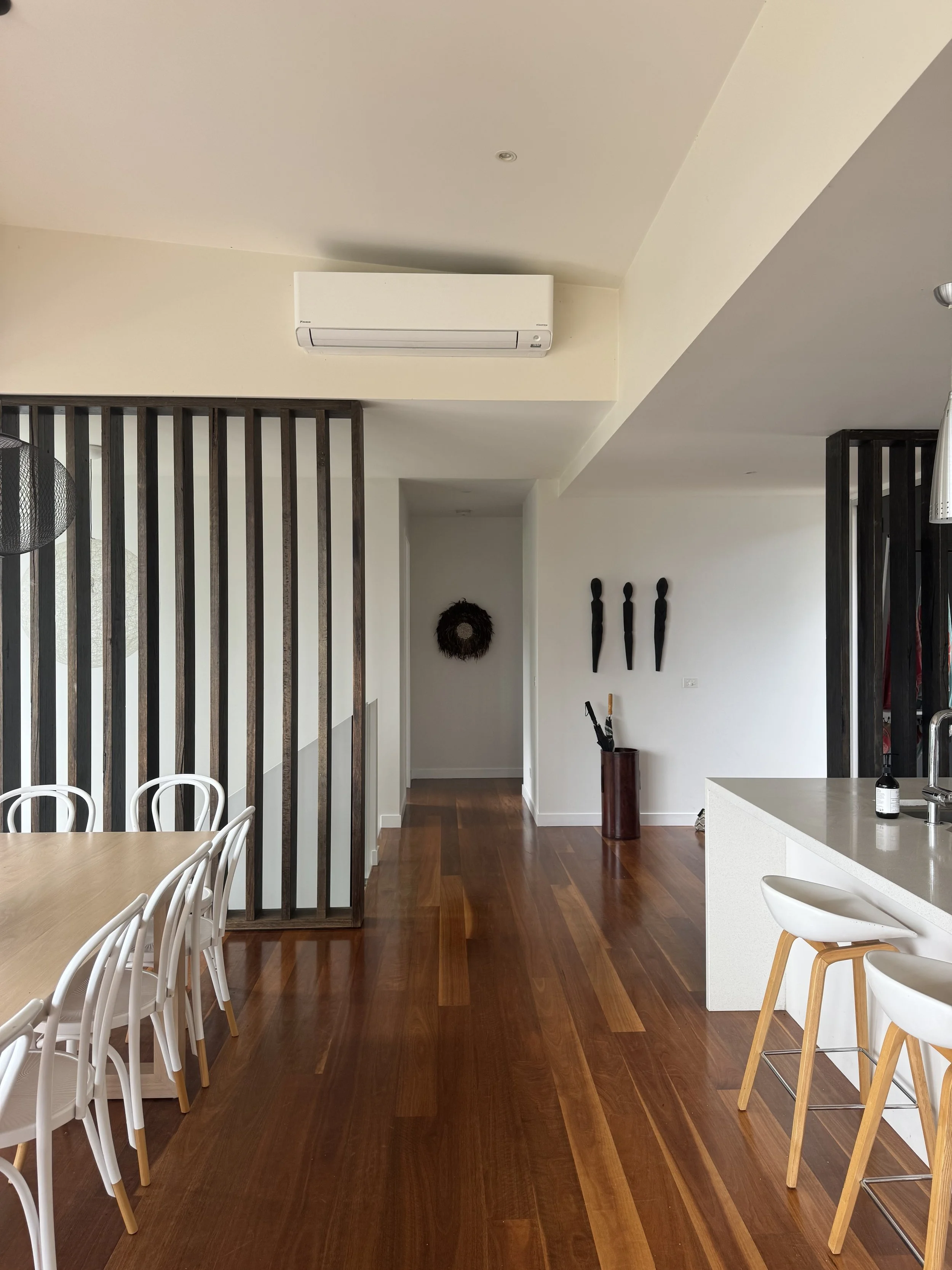 Modern kitchen and dining area with wooden flooring, white chairs, a wooden table, and black decorative wall accents.