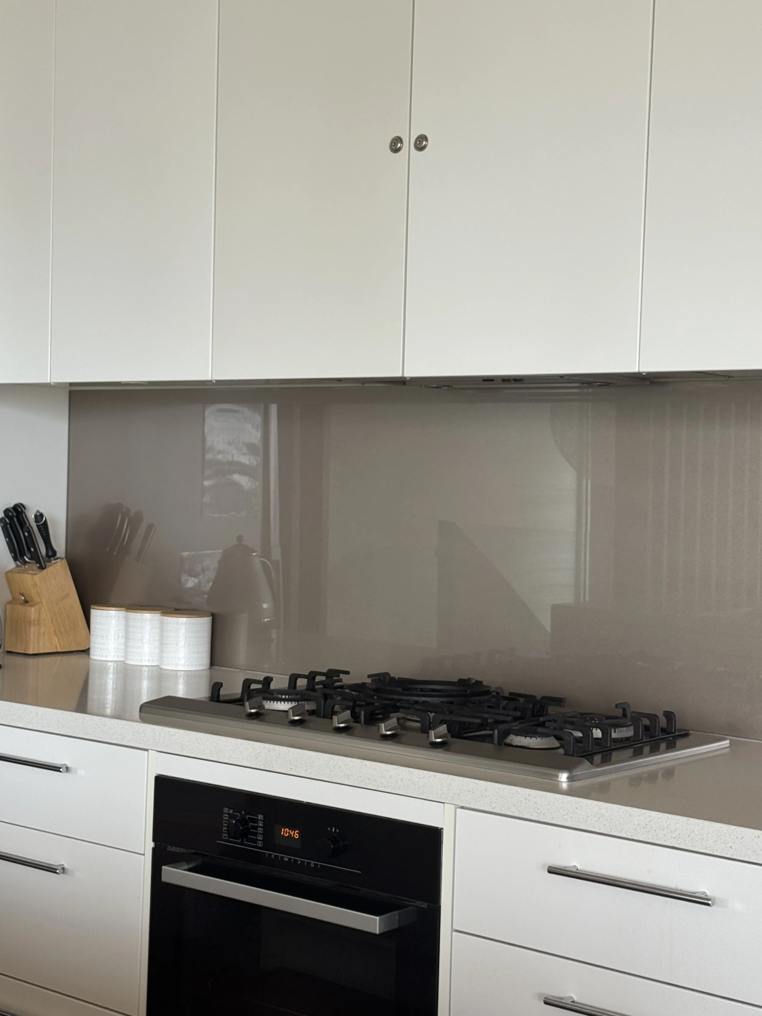 Modern kitchen with white cabinets, a gas stove, an oven, a knife block, and three cans on the countertop.