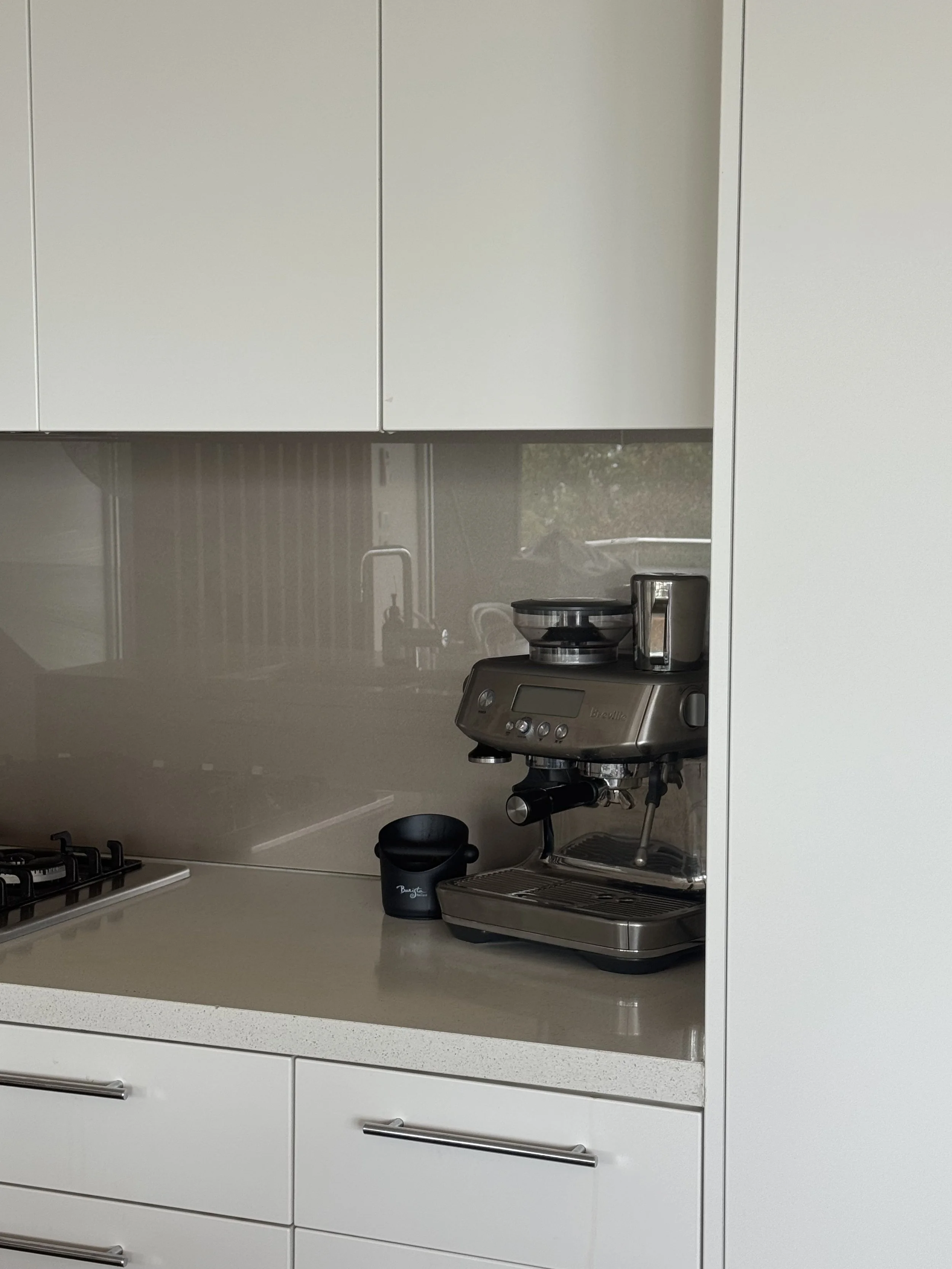 Kitchen counter with an espresso machine, a black mug, and a stainless steel kettle, with white cabinets above.