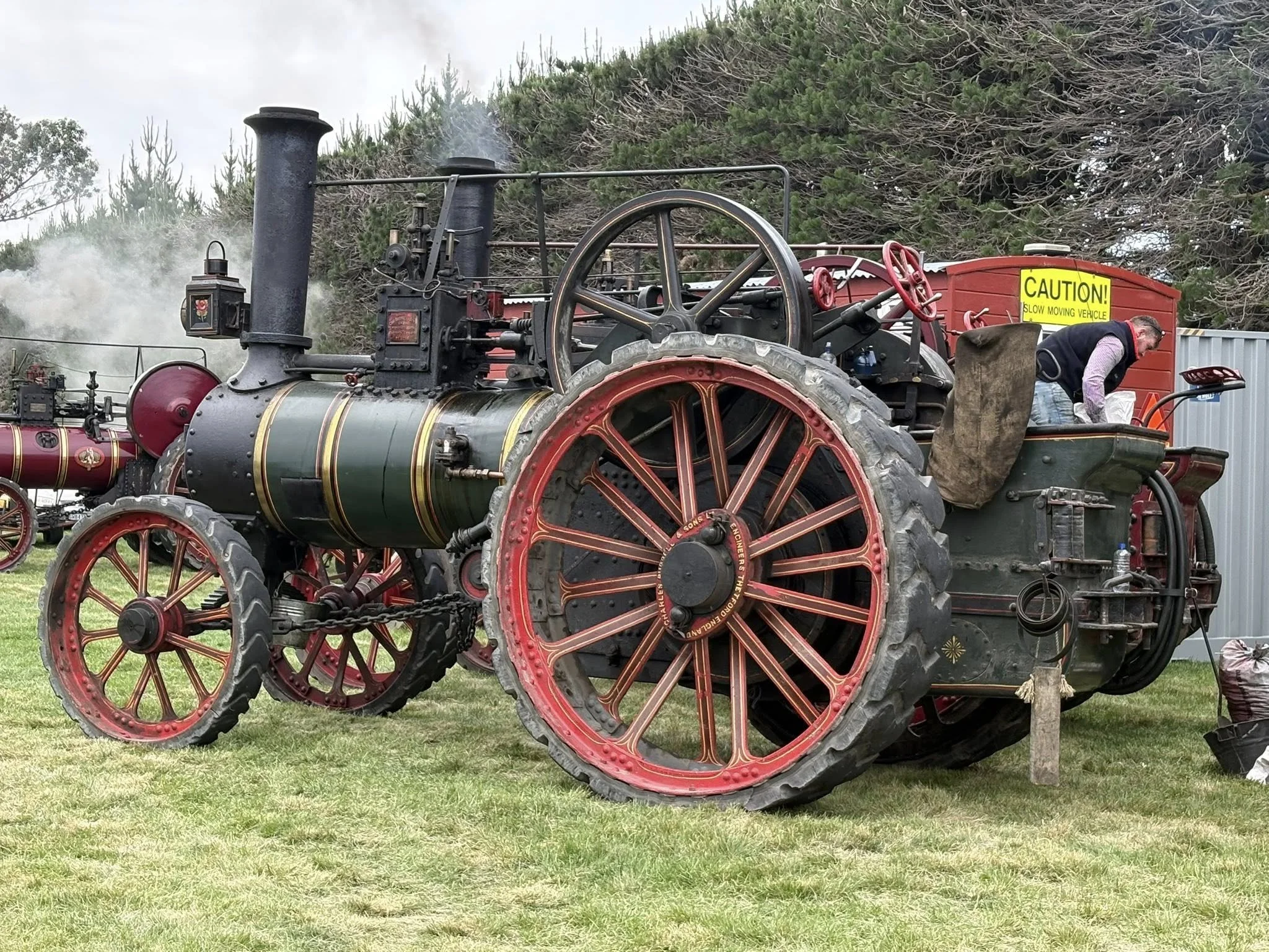 A vintage steam tractor with large red wheels and a black chimney, positioned on grass near trees.