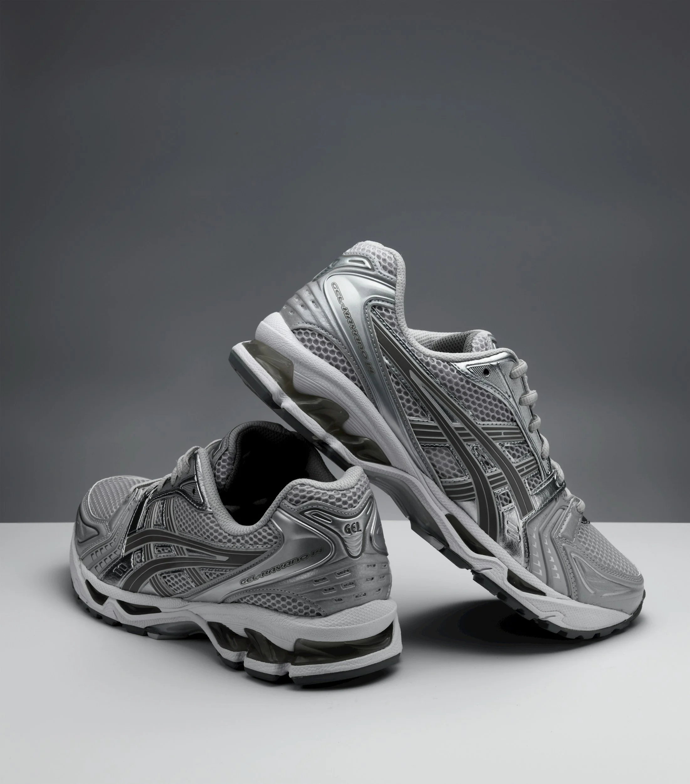 Two silver and gray athletic running shoes on a white surface against a gray background.