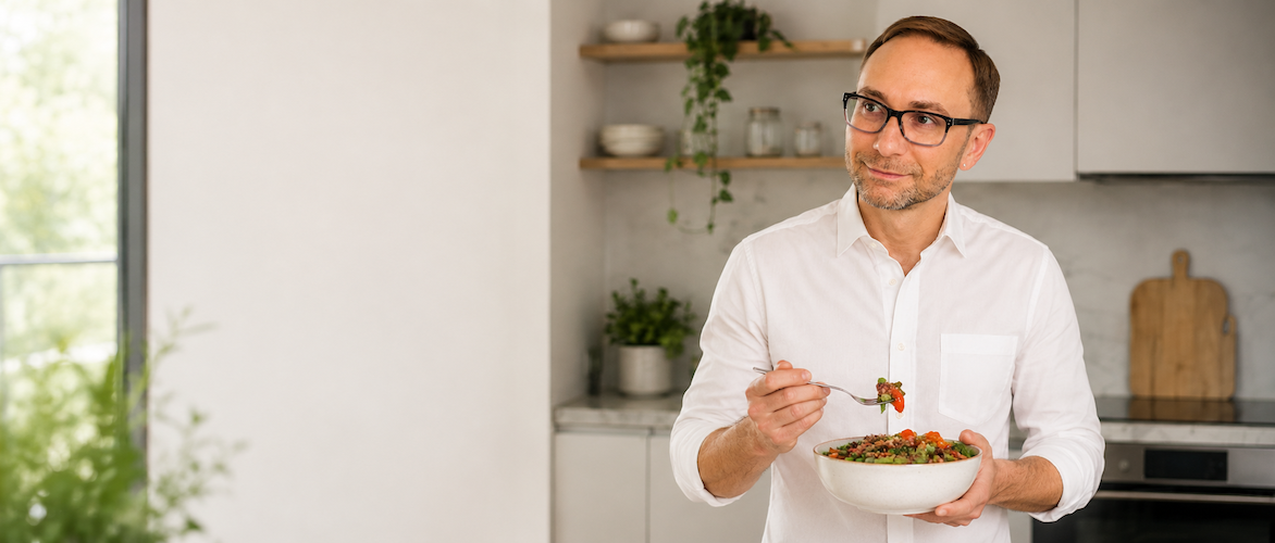 Alex Krasovsky holding a healthy meal in a modern kitchen, representing gut health coaching, digestion support, and real food habits.