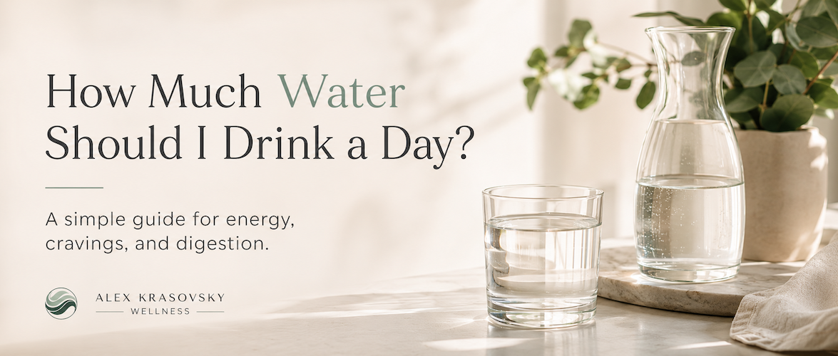 Glass of water and carafe in a bright wellness kitchen with text about how much water should I drink a day for energy, cravings, and digestion