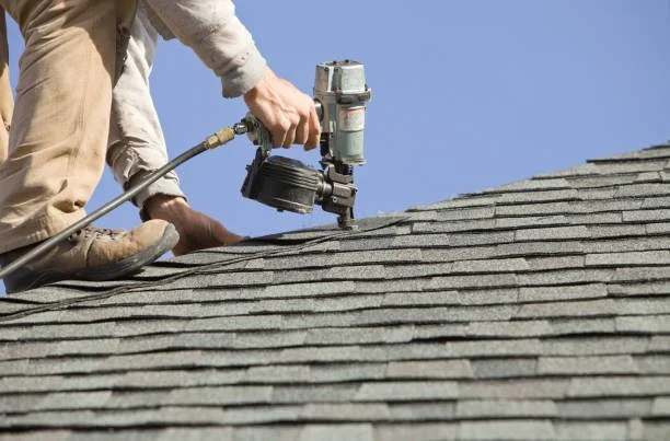 A worker using a pneumatic nail gun to nail down shingles on a roof.