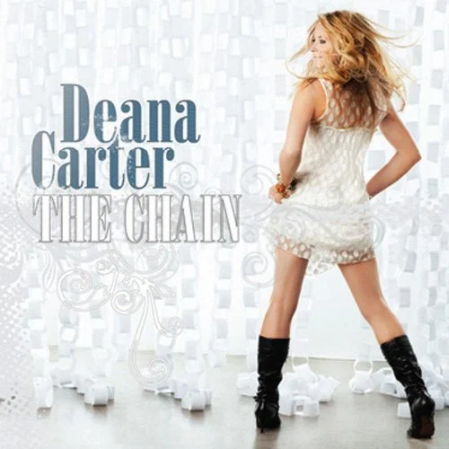 Deana Carter's album cover titled "The Chain" showing a woman with long blonde hair, wearing a short white dress and black boots, standing with her back to the camera amid scattered white chess pieces.