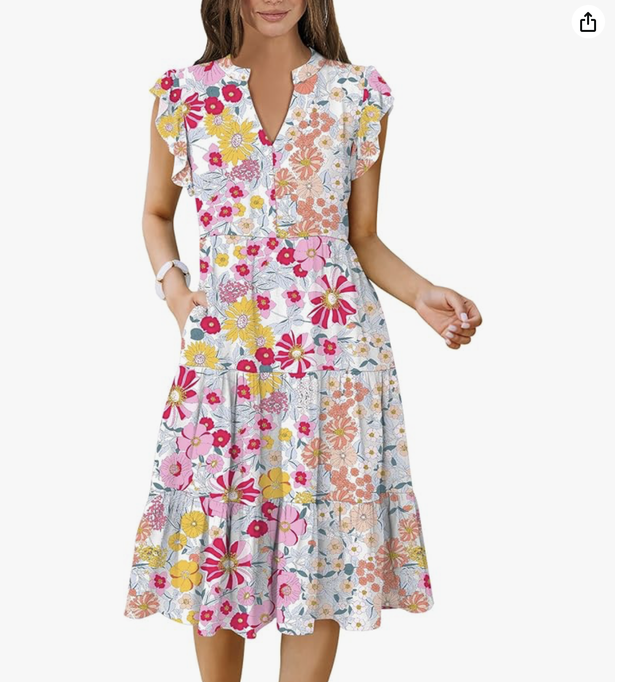 A woman wearing a sleeveless, floral maxi dress with ruffle details on the shoulders, featuring a colorful pattern of pink, yellow, orange, and white flowers.