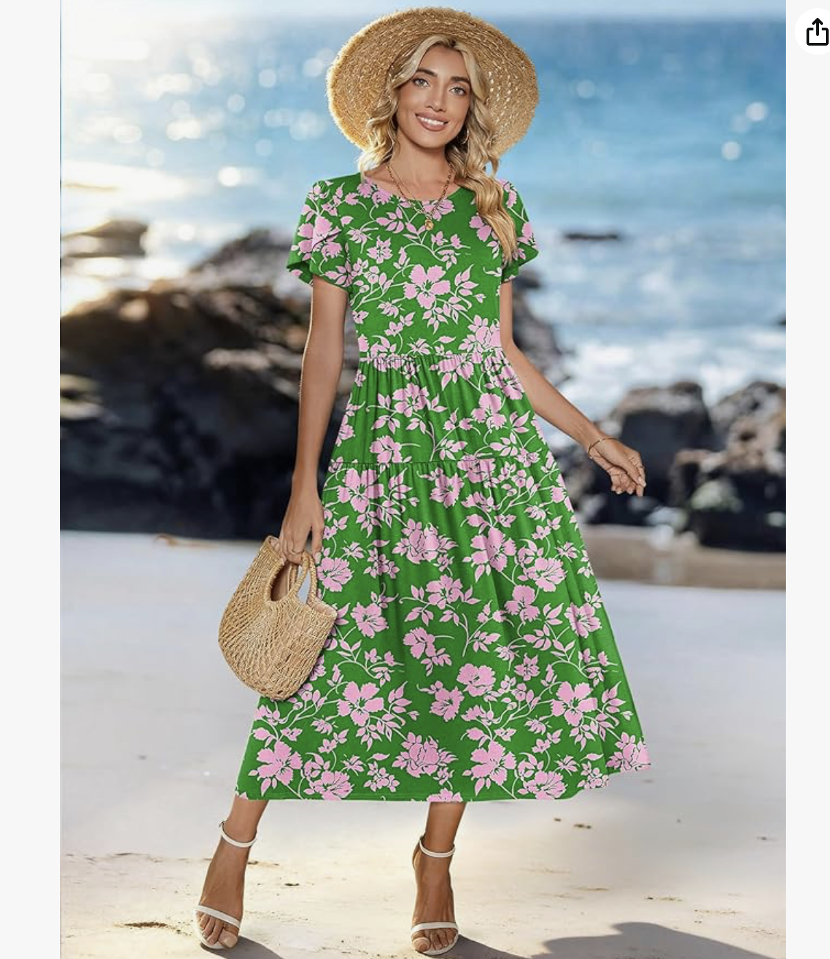 Woman wearing a green floral dress with pink flowers, a wide-brimmed straw hat, and white high-heeled sandals, standing on a beach with rocks and the sea in the background, holding a woven straw bag.