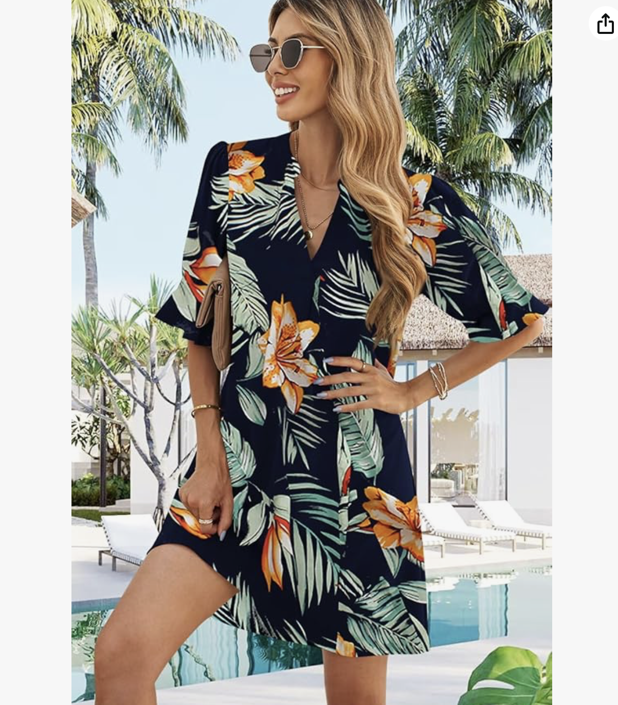 A woman in a floral dress standing by a swimming pool with palm trees in the background.