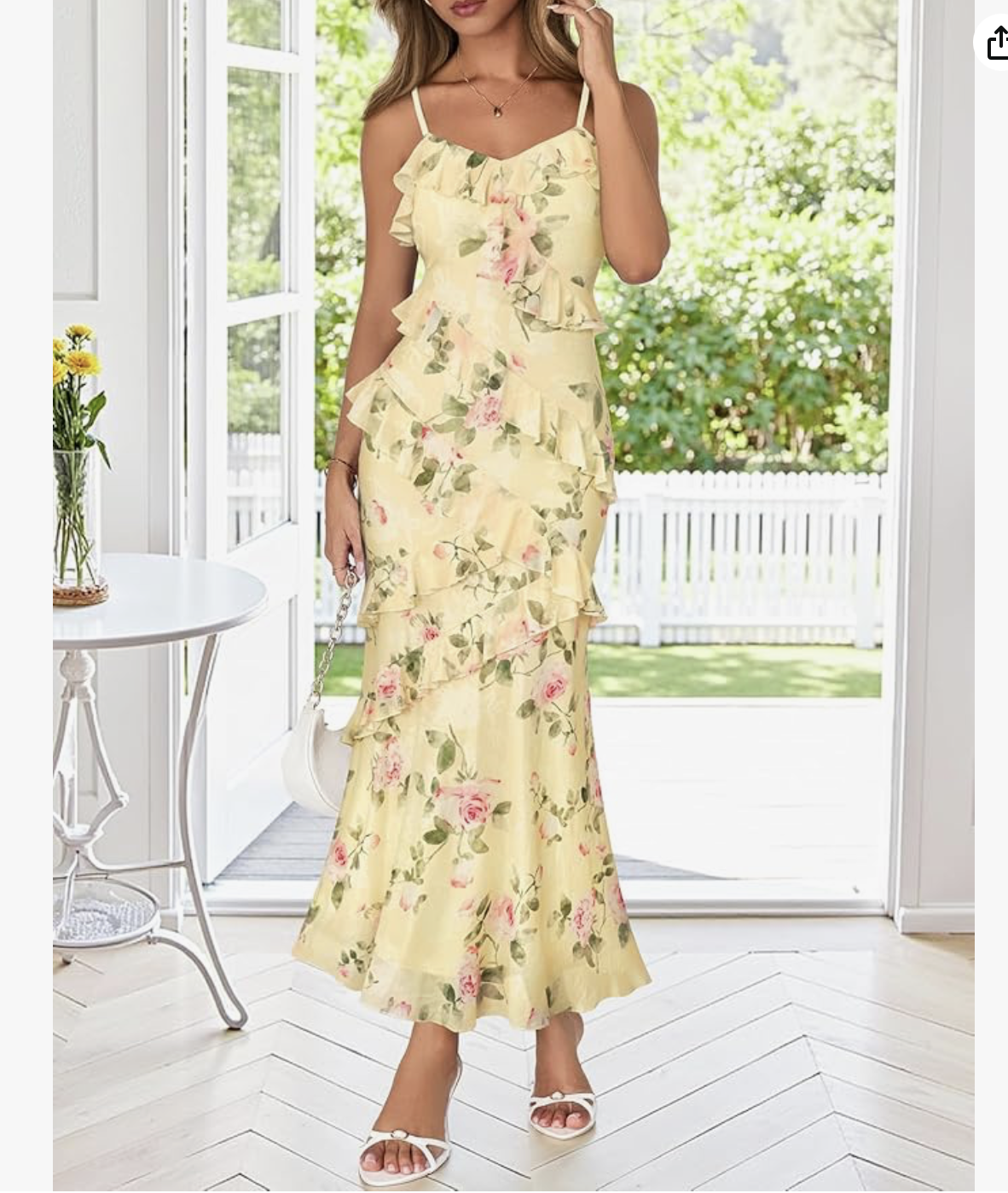 A woman wearing a yellow floral dress with ruffles standing indoors near an open door with a garden outside.