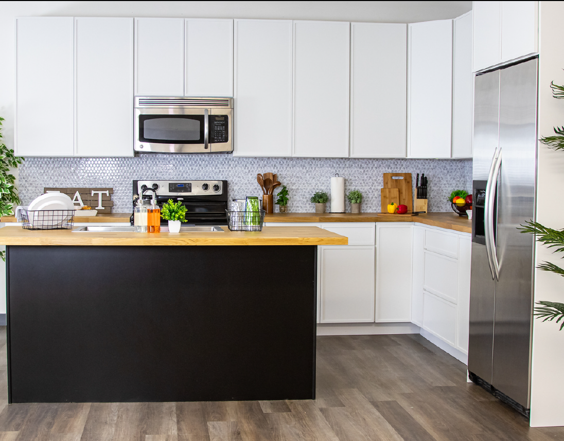 Modern kitchen with white cabinets, stainless steel appliances, a black and wood-tone island, and various kitchen items and decor on the countertops.
