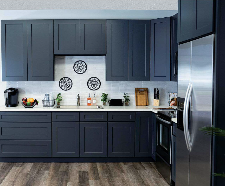 Modern kitchen with navy blue cabinets, a stainless steel refrigerator, black stove, white tiled backsplash, and various kitchen items on the counter.