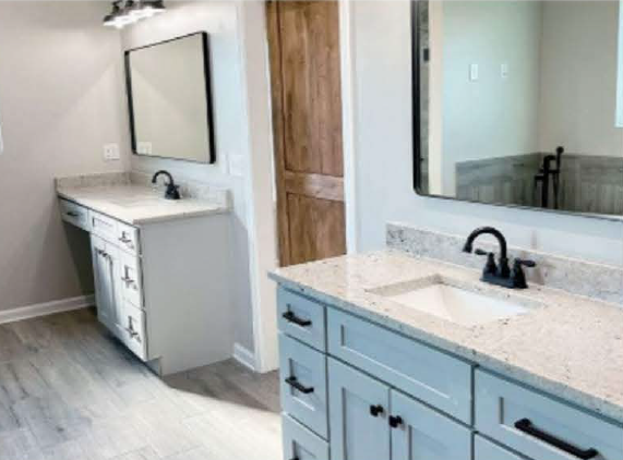 Bathroom with two vanities, one white and one blue, each with a black faucet and a large mirror, and a wooden door in the background.