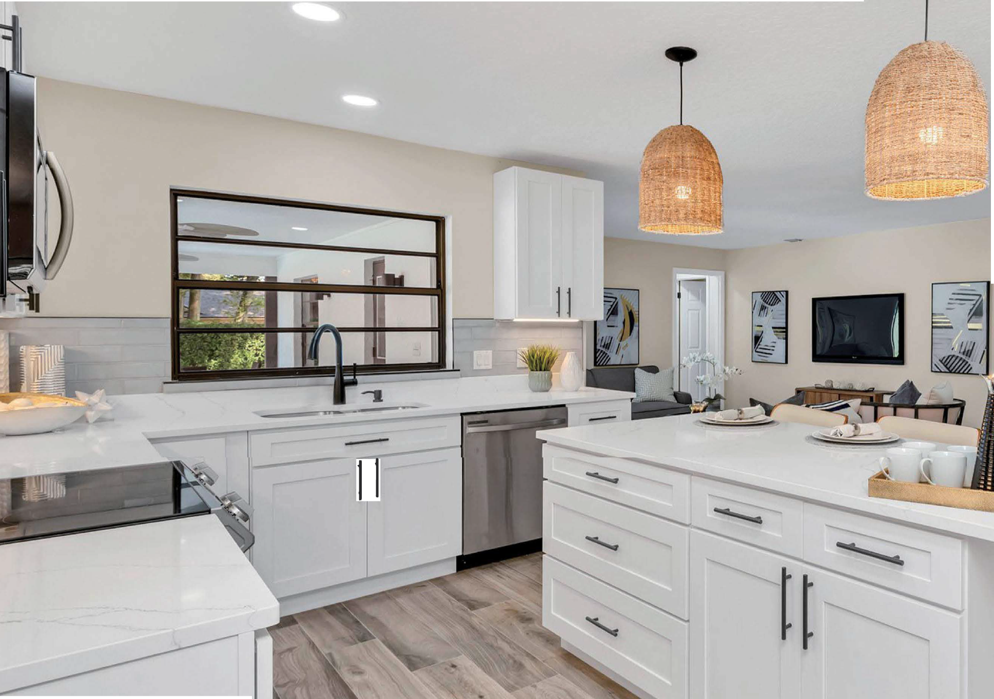 Modern kitchen with white cabinets, marble countertop, black sink, hanging wicker pendant lights, and a view into the living room with wall art and a TV.