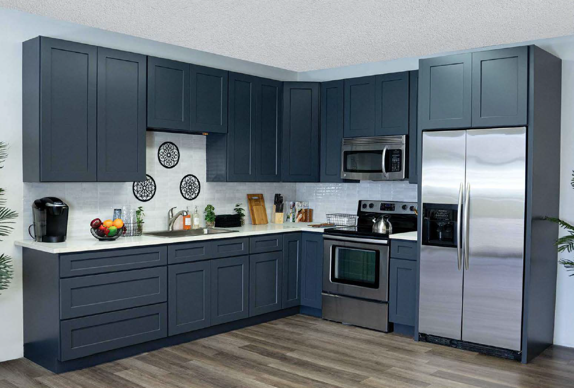 Modern kitchen with navy-blue cabinets, stainless steel appliances including a refrigerator, microwave, and oven, white tiled backsplash, and wood flooring.