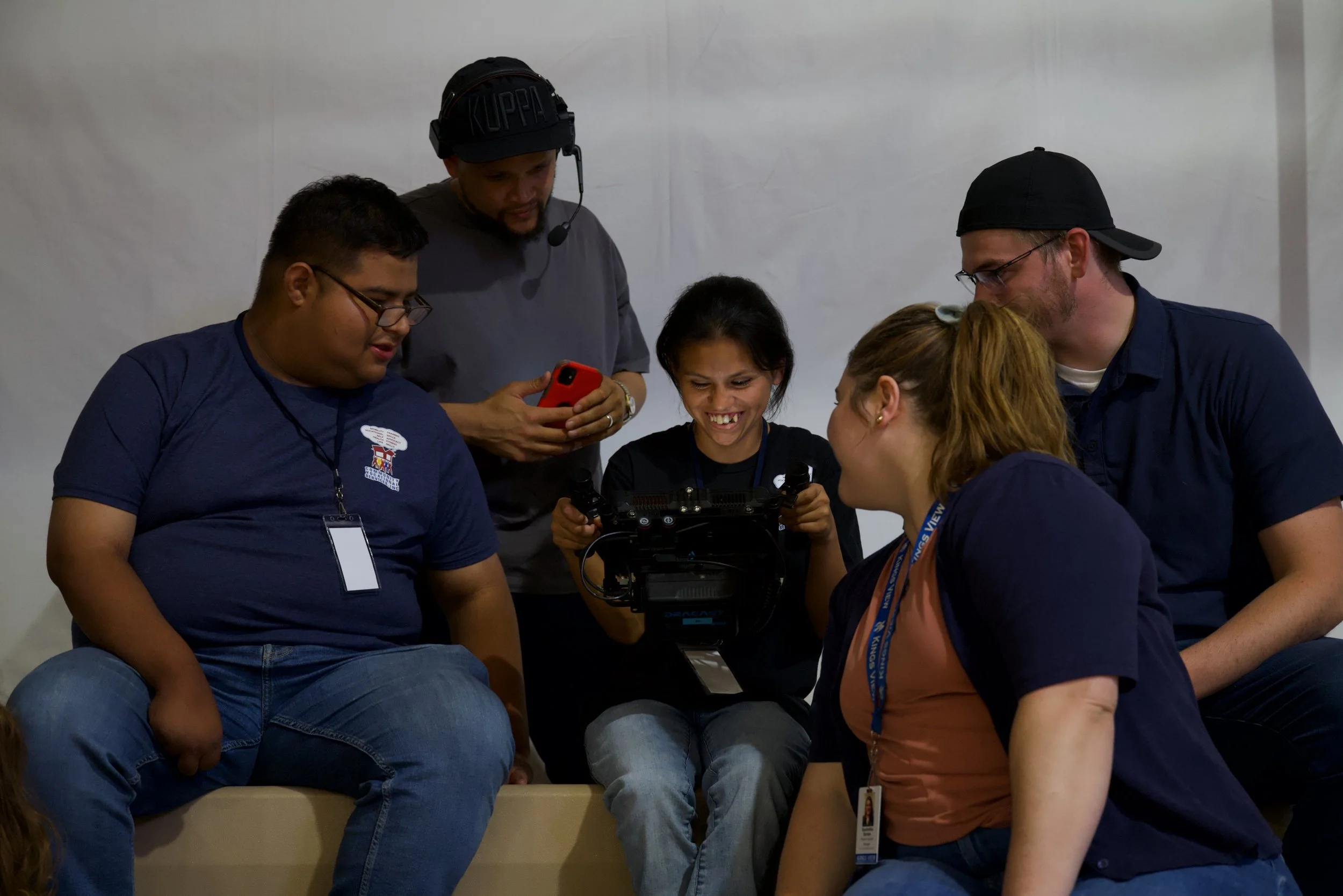 A group of six diverse individuals gathered around a camera, looking at its screen and engaging with each other in a casual setting.