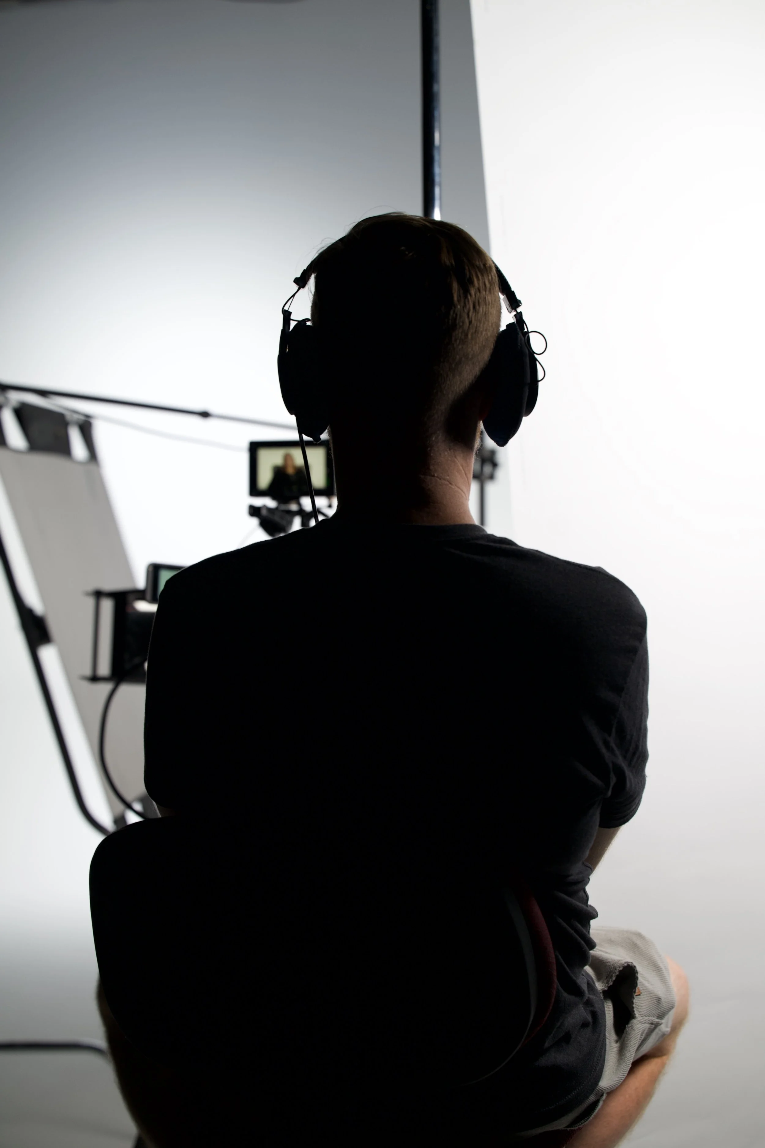 Person wearing headphones sitting in front of camera and lighting equipment in a studio.