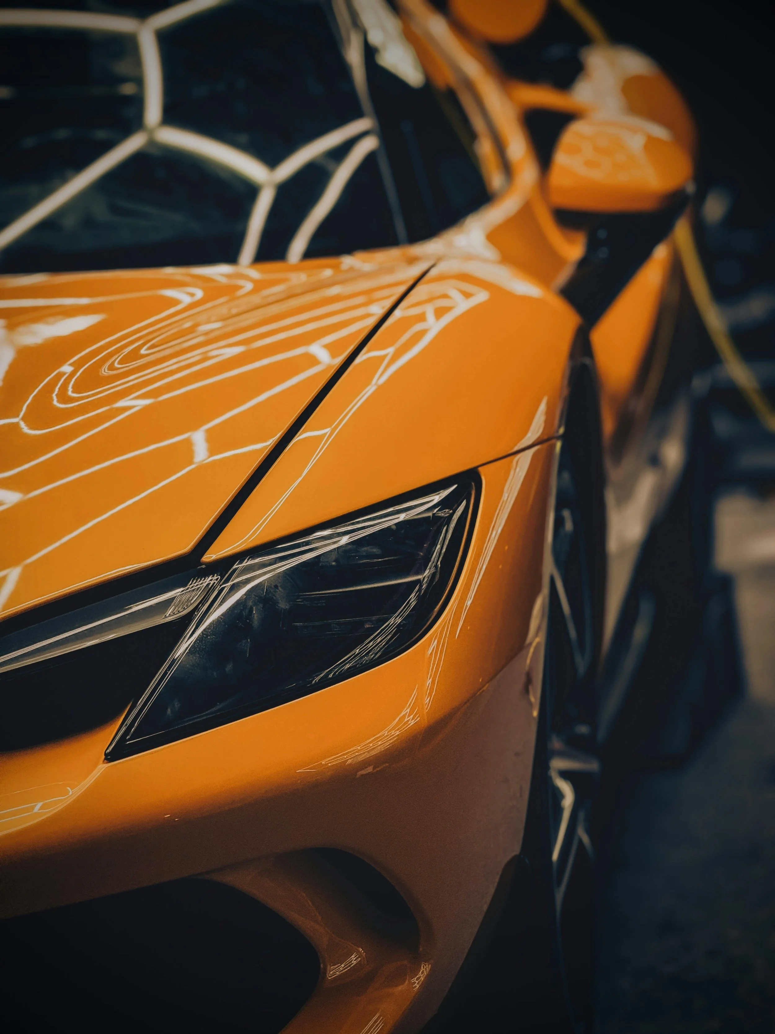 Close-up of a bright orange sports car with black accents, showing its sleek, aerodynamic design and sharp headlight.