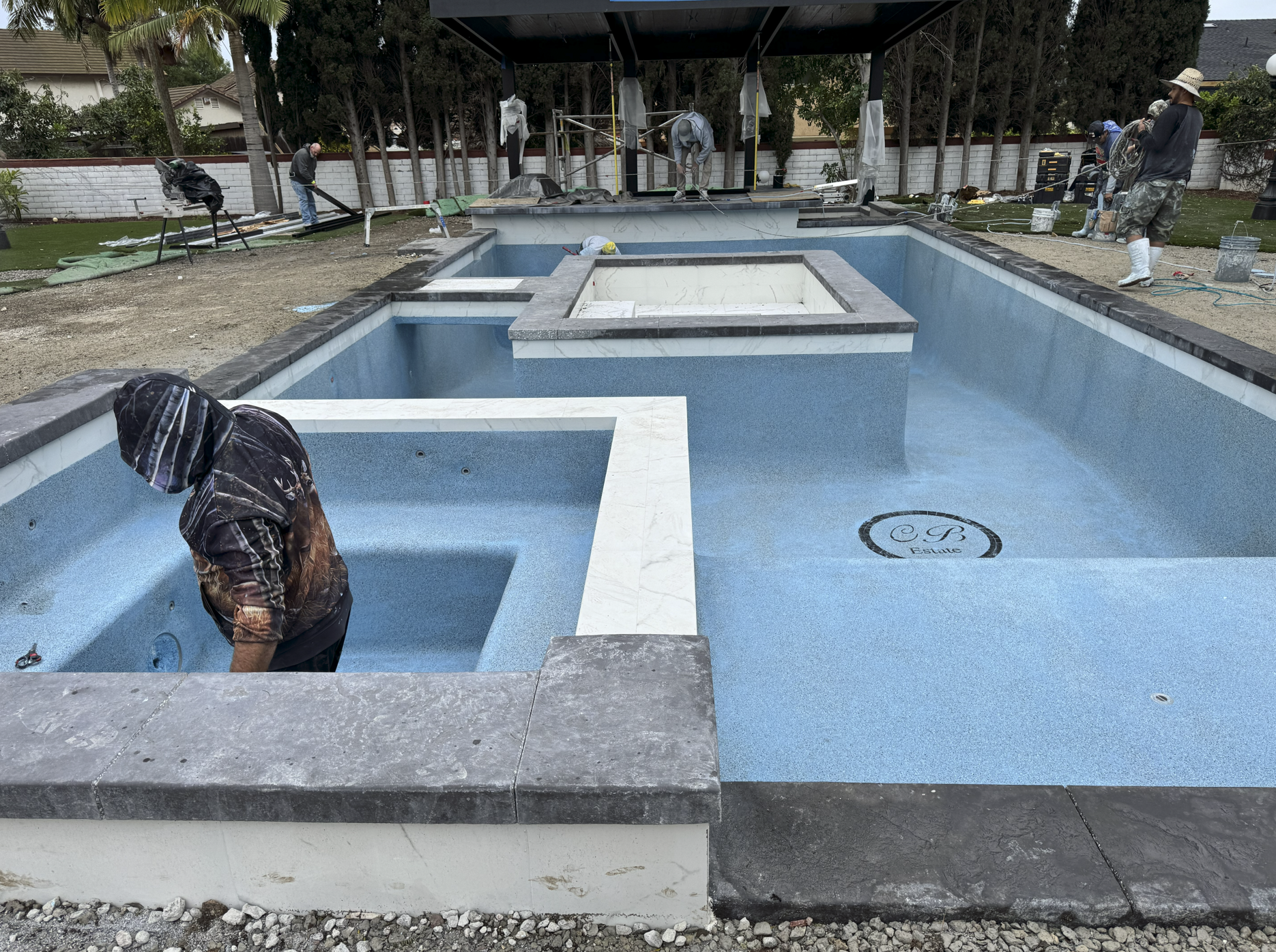 Construction workers renovating a residential swimming pool with the pool partially filled with water and some workers inside and around it.