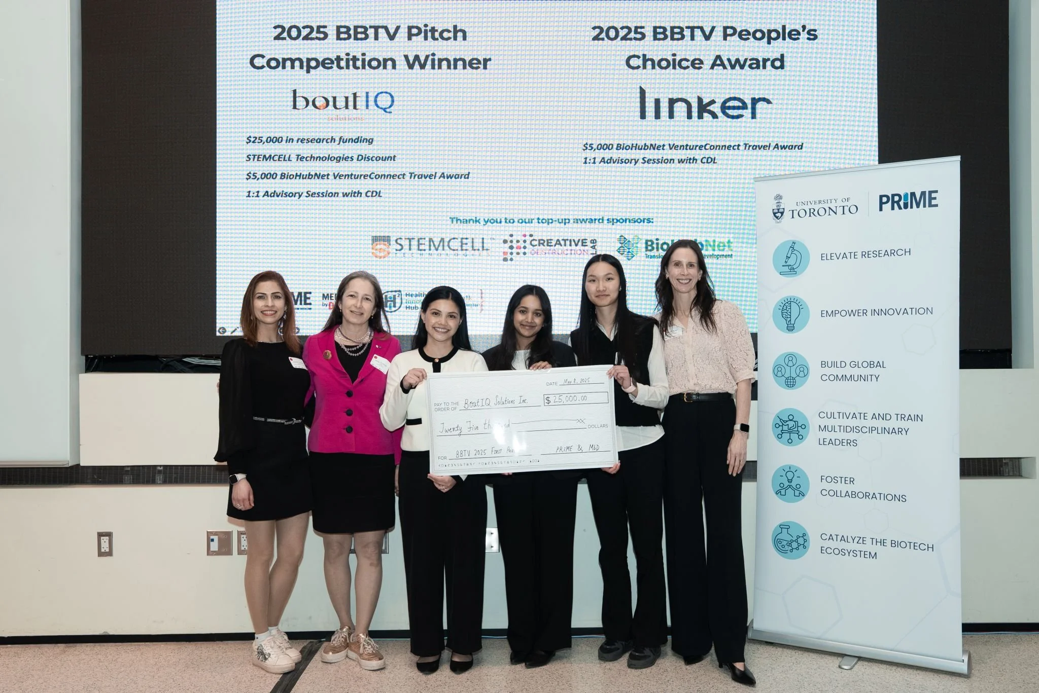 Group of six women standing in front of a large digital screen, holding a giant check for $25,000 awarded to BoutIQ Solutions Inc. for winning the 2025 BBTV Pitch Competition and People's Choice Award