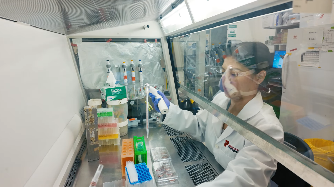 A scientist working in a laboratory fume hood, wearing safety glasses and gloves, using a pipette for experiments.