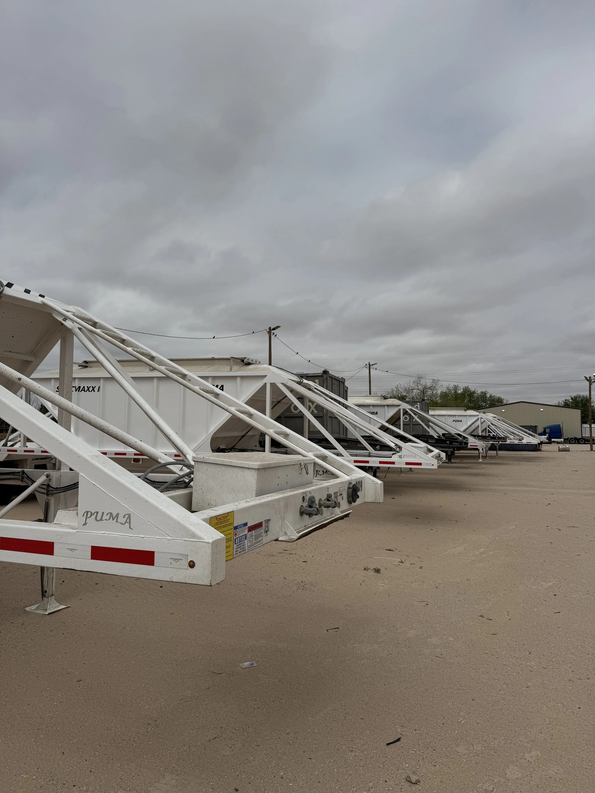 Several white trailers parked in a lot under a cloudy sky, with some power lines and a small building in the background.