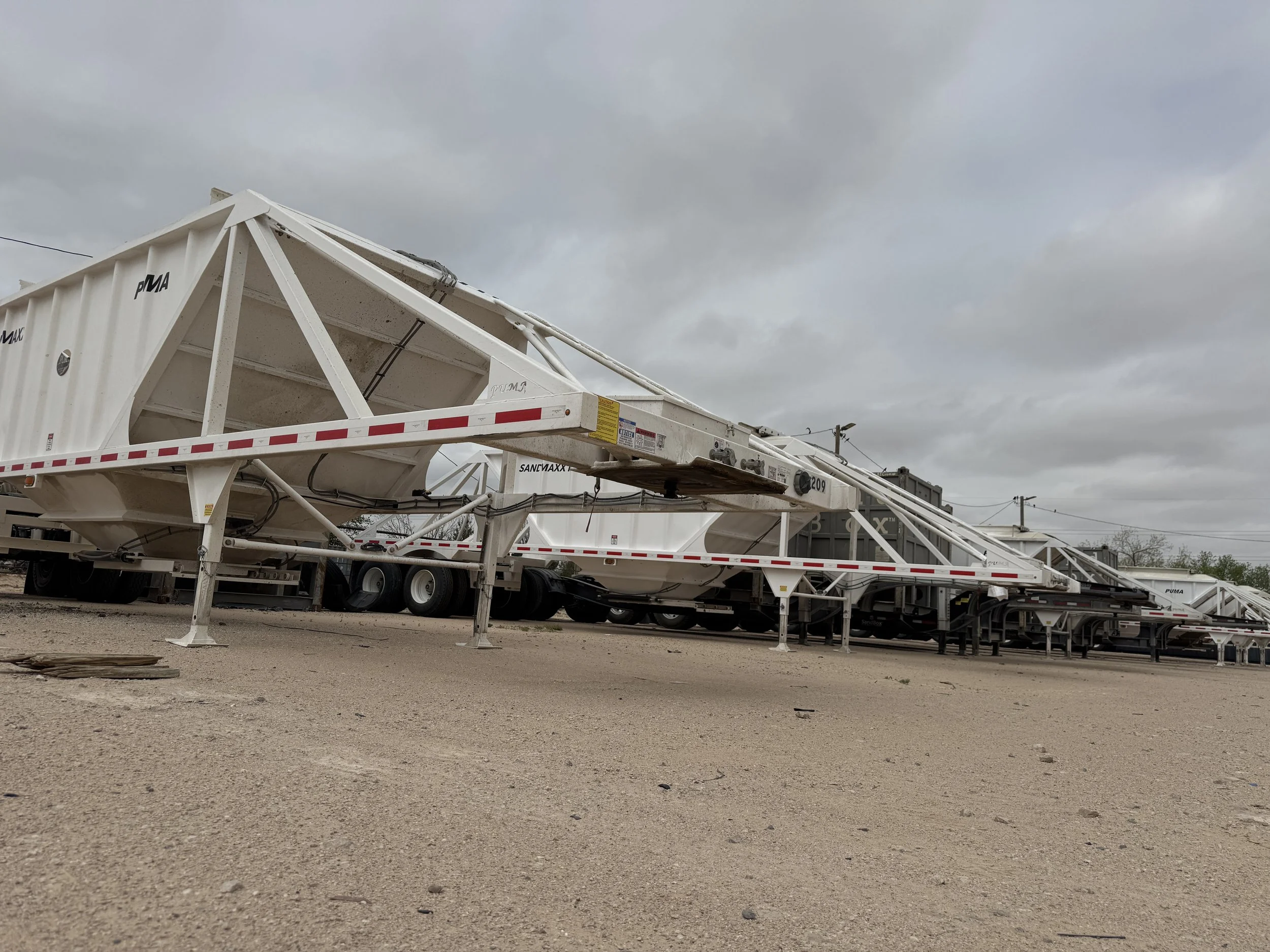Multiple white mobile conveyor belt structures parked on a gravel lot under a gray cloudy sky.