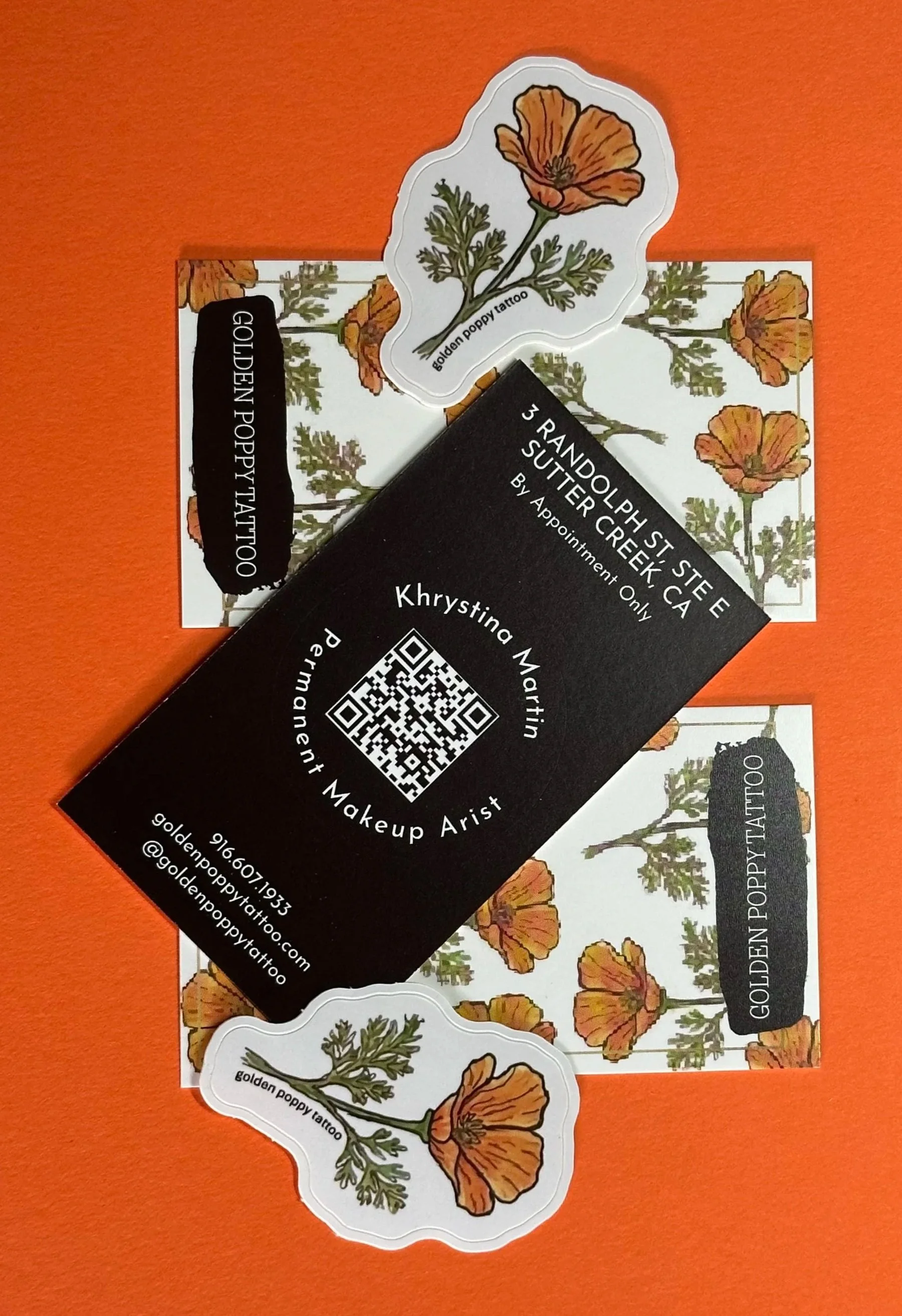 Business cards displaying the name Krystina Martin, occupation of permanent makeup artist, with contact details, and featuring a poppy flower illustration. There are also stickers with the same poppy flower image and text 'golden poppy tattoo,' placed on a floral-themed background paper.