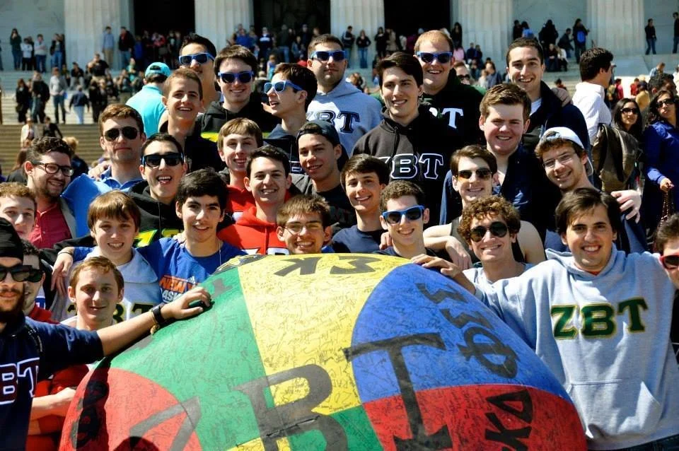Fraternity brothers posing with a colorful philanthropy ball outside.