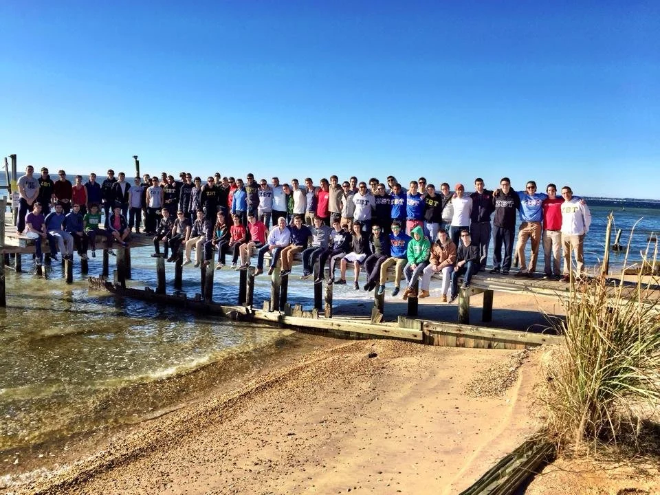 Fraternity brothers gathered on a wooden pier by the water.