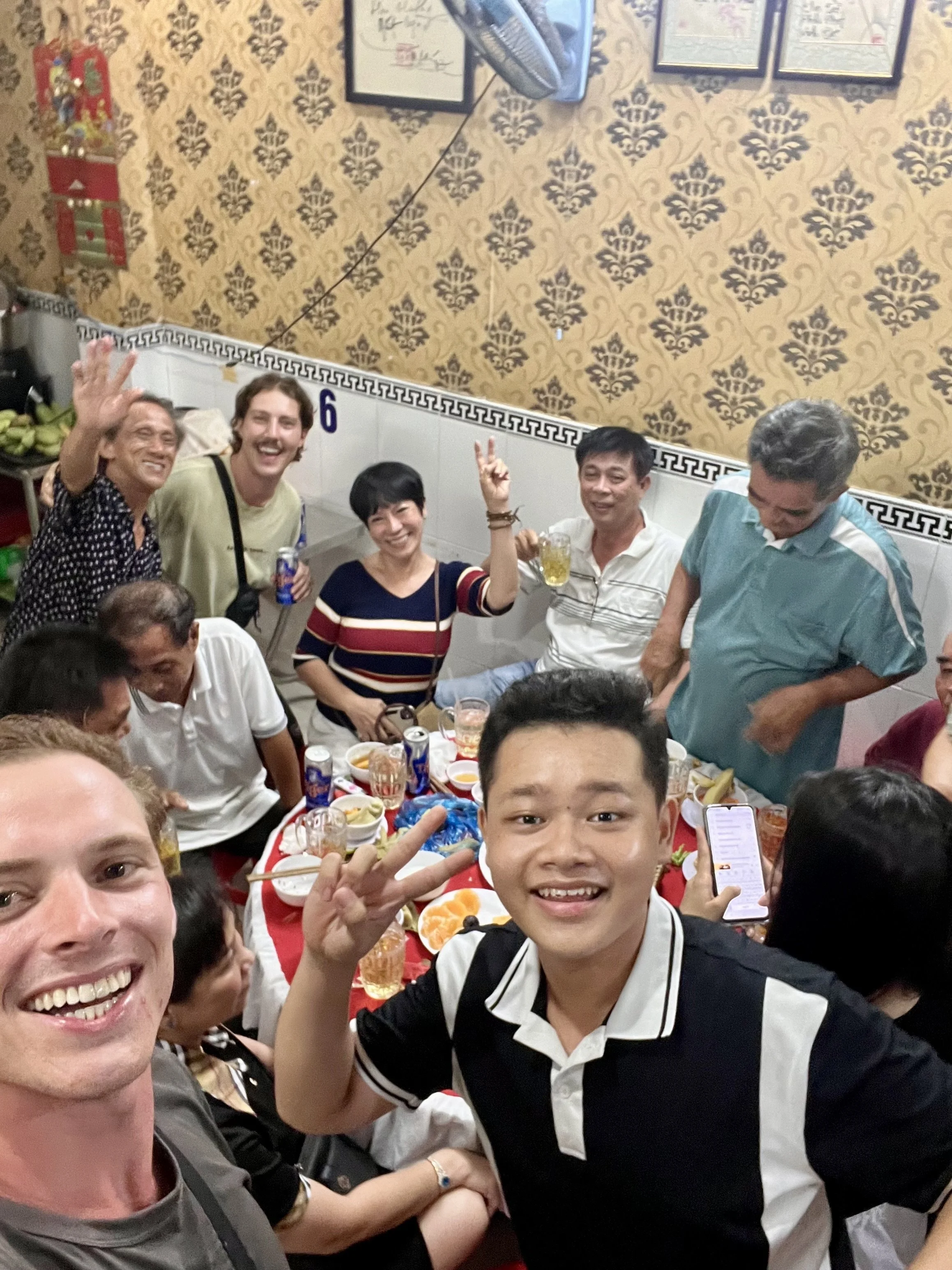 A group of people celebrating at a gathering with food and drinks, smiling and making peace signs.