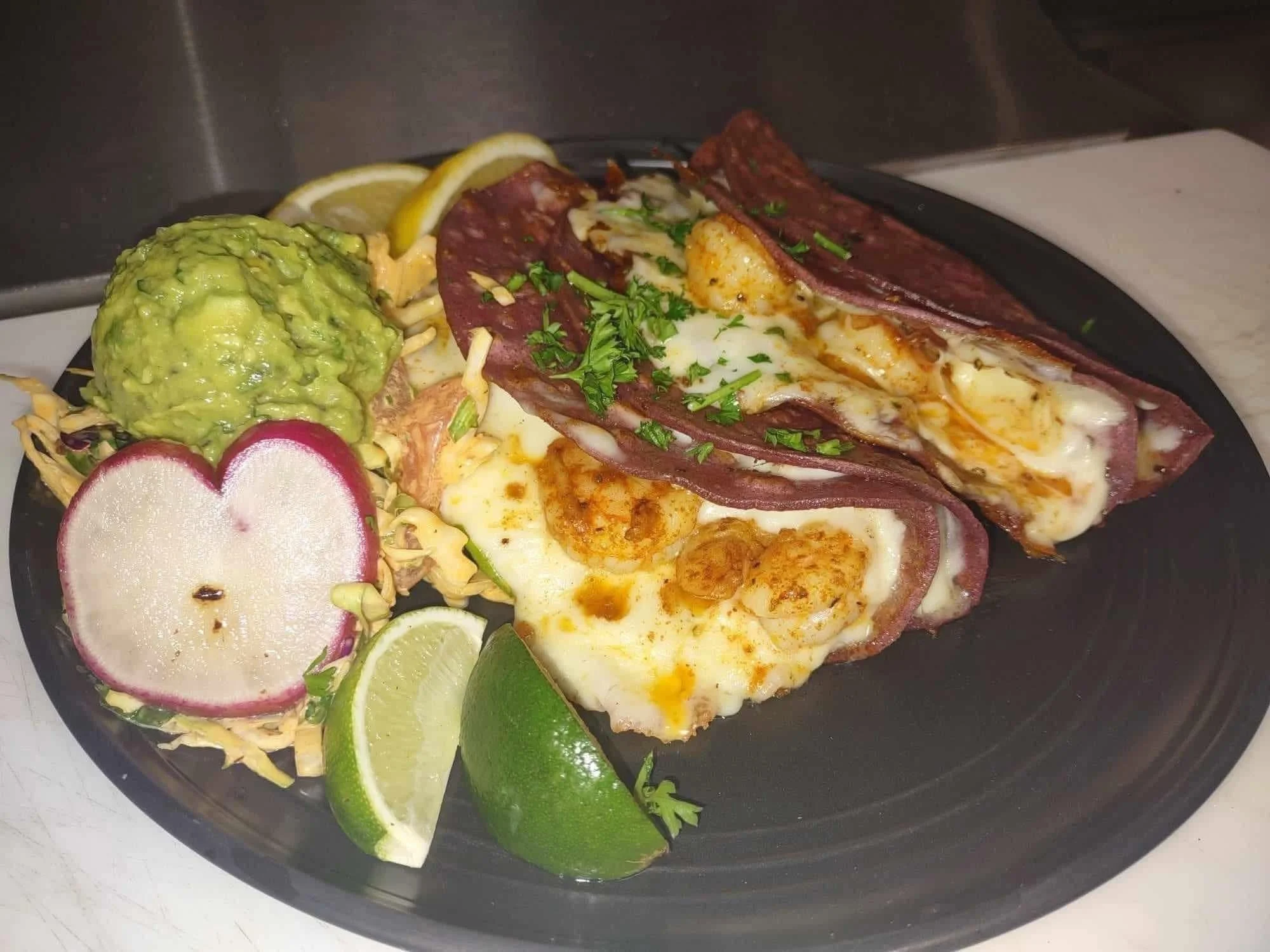 Served Mexican breakfast plate with two ham and egg tacos garnished with chopped cilantro, avocado, lime wedges, shredded lettuce, radish slices, and lemon wedges.