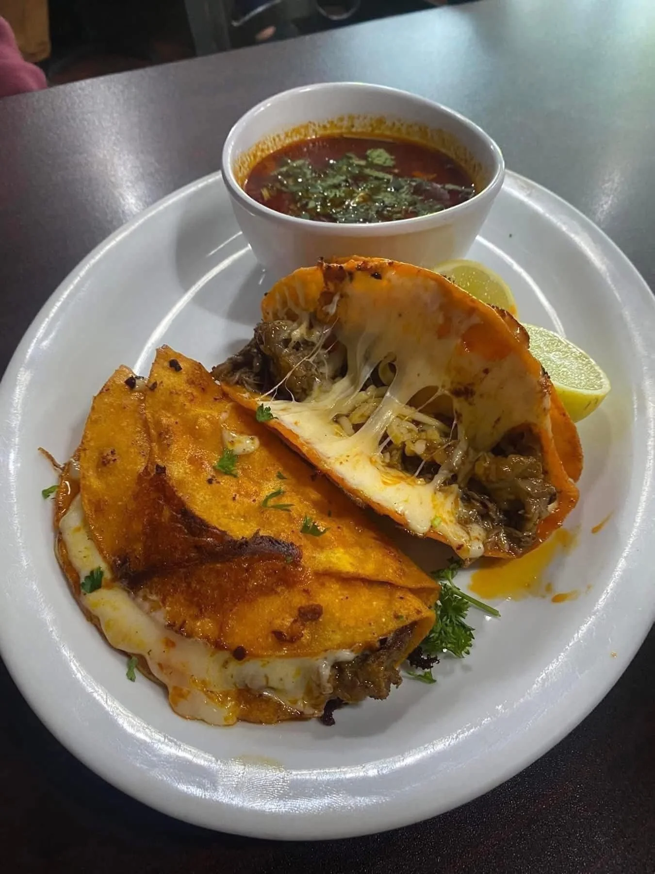 A plate of Indian cuisine featuring a stuffed naan bread with cheese and vegetables, served with a side of spicy soup garnished with herbs and lemon wedges.